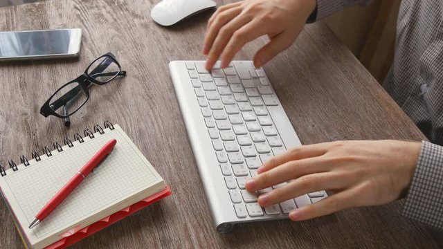 Man arms typing on keyboard at natural hardwood desk