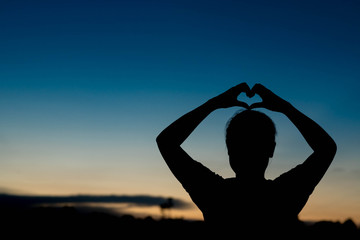 silhouette of woman Hand-made heart-shapedon on sky at sunset.