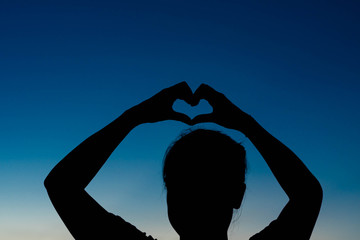silhouette of woman Hand-made heart-shapedon on sky at sunset.