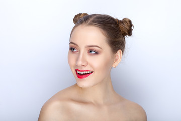 Naklejka premium Portrait of a young pretty woman with trendy makeup bright red lips funny bun hairstyle and bare shoulders act the ape against white studio background