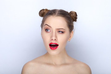 Portrait of a young pretty woman with trendy makeup bright red lips funny bun hairstyle and bare shoulders act the ape against white studio background