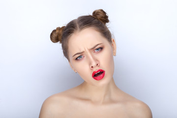 Portrait of a young pretty woman with trendy makeup bright red lips funny bun hairstyle and bare shoulders act the ape against white studio background