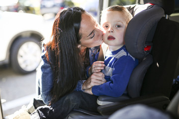 Mother securing her boy in the car seat in