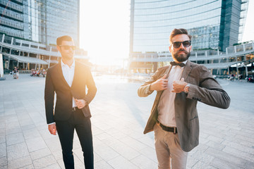 Two young bearded blonde and black hair modern businessman, posing outdoor in the city back light...