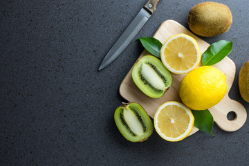 Lemons and kiwis fruits with knife and wood cutting board are on - obrazy, fototapety, plakaty