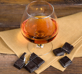 Glass of brandy and a chocolate on wooden table