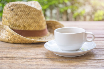 coffee brake - coffee cup  with straw hat background on wooden table in the morning warm light.