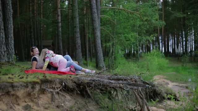 A pregnant woman is lying on a red blanket in the woods and enjoy nature.