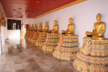 Golden Buddhist statues on colored pedestals in a long corridor