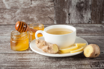 A white cup of green natural tea with ginger, lemon and honey on wooden rustic background. Healthy drink. Hot winter beverage concept.