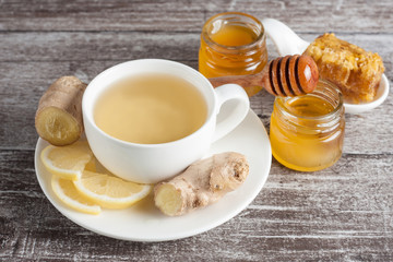 A white cup of green natural tea with ginger, lemon and honey on wooden rustic background. Healthy drink. Hot winter beverage concept.