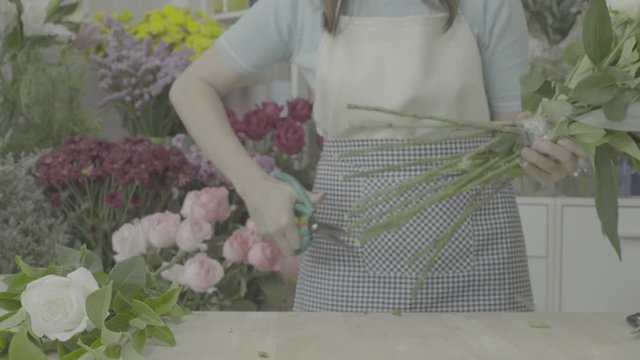 Florist woman trimming stems of a beautiful flower bouquet with scissors, ungraded tone