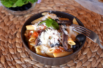 Delicious italian food penne ala puttanesca on a bowl on a table.
