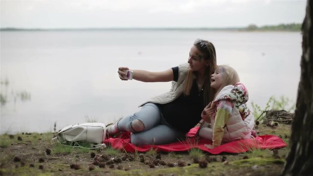 Pregnant woman and her daughter making selfie on on a picnic near the lake.