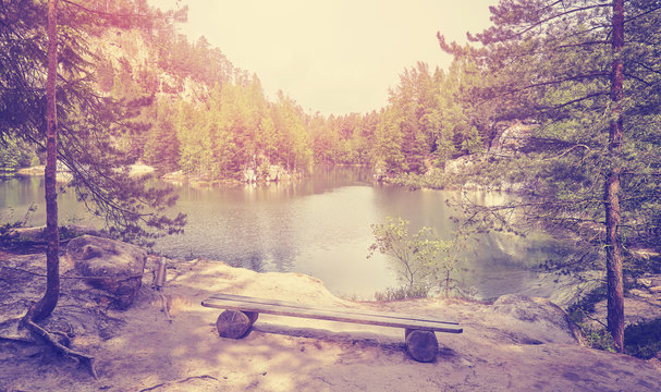 Vintage toned photo of a bench by a mountain lake.