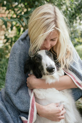 Young woman embracing her dog under a warm blanket