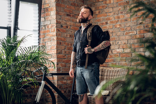 Tattooed hipster male in a room with bicycle on background.