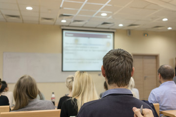 Rear view of students attentively listening to the teacher near the white board