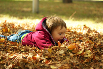 Cute little girl lies in the leaves in an autumn park