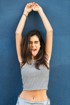 brunette girl in crop top with arms up showing tongue at camera