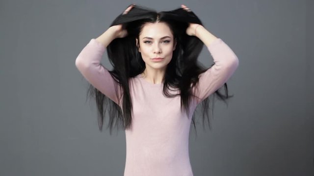 Young beautiful brunette woman is stroking the hair and playing with it, gray background