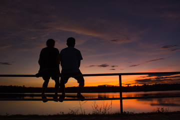 Fototapeta na wymiar silhouette man and woman couple sitting on the iron bar at sunset