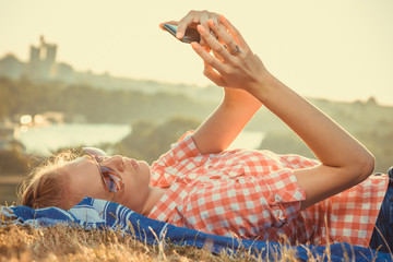 Young trendy woman lying on field above the city and taking selfie. Summer, vacation and technology concepts.