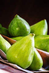 Sweet green figs in bowl, wooden background, selective focus