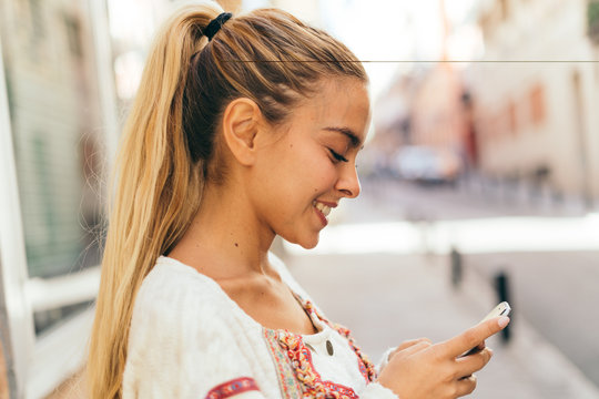Happy young woman using mobile phone in the street