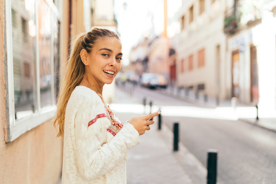 Happy young woman using mobile phone in the street