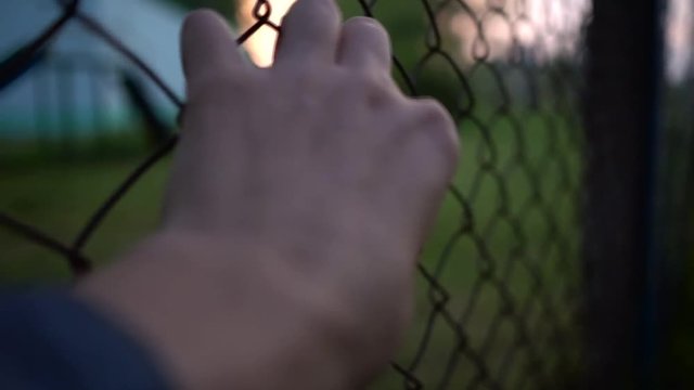 Helpless man's hand shake A Metal Fence Trying To Escape. Sunset infront. Evening. Hope