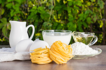 Лапша на фоне куриных яиц, муки, молока, масла и кувшина на деревянном столе