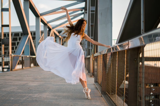 Attractive ballerina in white dress on metal construction