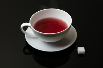 Tasse Tee mit Würfelzucker vor schwarzem Hintergrund