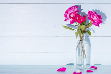 Pink roses in a vase on a blue wooden background.  Greeting card concept. Wedding invitation.
