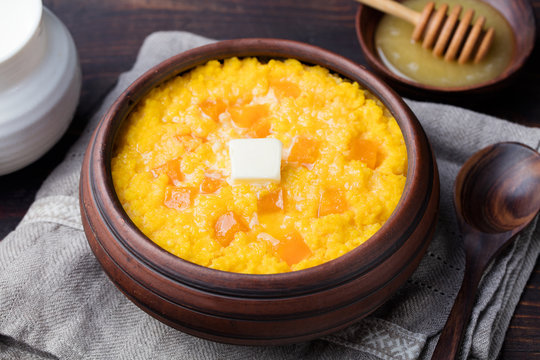 Millet porridge with pumpkin in a clay bowl on a rustic wooden background.