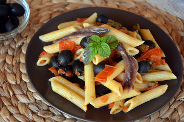 Delicious italian pasta penne with anchovies on a plate on a table.