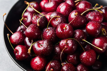 Fresh ripe black cherries in a black bowl on a grey stone background Close up