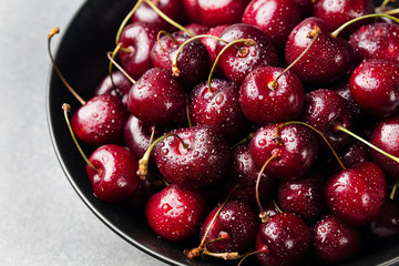 Fresh ripe black cherries in a black bowl on a grey stone background Close up