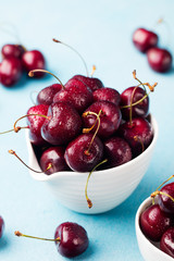 Fresh ripe black cherries in a white bowl on a blue stone background