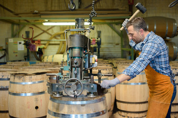 cooper at work hammering top on to wooden barrel
