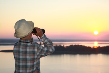 Obraz premium мальчик смотрит в бинокль на восход солнца на реке