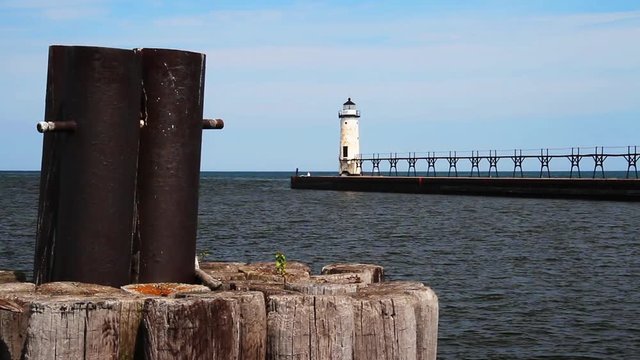 Loop features the white lighthouse at Manistee, Michigan and its long elevated catwalk approach with a piling of weathered timbers in the foreground. Lake Michigan 