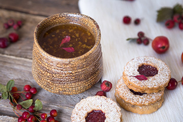 Fototapeta premium Autumn tea time. Clay mug of tea with cookies on a wooden background decorated with autumn berries and oak leaves. 