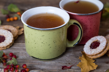 Autumn tea time. Two mugs of tea with cookies on a wooden background decorated with autumn berries and oak leaves. 