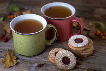 Autumn tea time. Two mugs of tea with cookies on a wooden background decorated with autumn berries and oak leaves. 