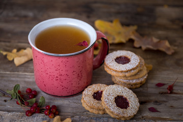 Autumn tea time. Red mug of tea with cookies on a wooden background decorated with autumn berries and oak leaves. 