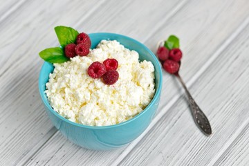 Cottage cheese in blue bowl with raspberries and mint on wooden background napkin