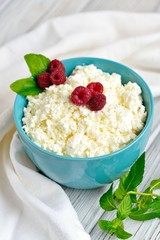 Cottage cheese in blue bowl with raspberries and mint on wooden background