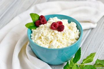 Cottage cheese in blue bowl with raspberries and mint on wooden background
